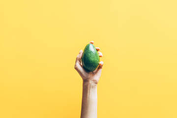 Wall Mural - Top view of woman hand holding avocado on yellow background.