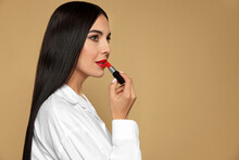 Beautiful young woman applying red lipstick on beige background, space for text