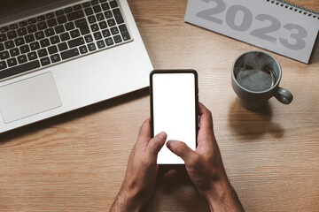 Unrecognizable man holding a smartphone with a blank screen, a laptop and a hot coffee - concept goals and action plan, new year