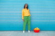© VISTA by Westend61 - Young woman standing with basket full of oranges in front of blue wall