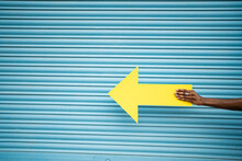 Hand Of Man Holding Yellow Arrow Sign In Front Of Blue Shutter