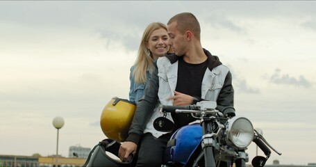 Wall Mural - A young stylish couple of bikers sit on a bike standing in a public city parking. The guy and the girl put on motorcycle helmets. Love and safety