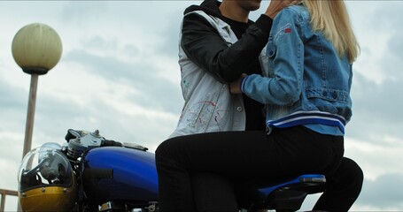 Wall Mural - Close-up of a young stylish couple of bikers meet and hug near a motorcycle standing in a public city parking lot.