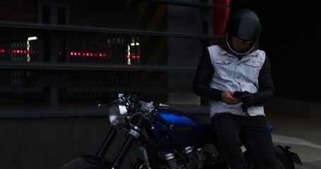 Close-up of a motorcyclist sitting on a motorcycle writing a text on a smartphone watching the news. Biker flipping through social networks in the phone sending a message