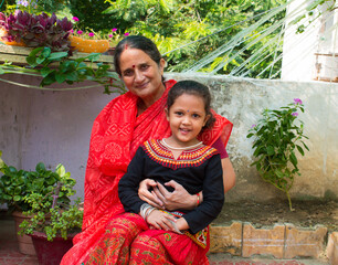 A grand daughter sitting on the lap of Grand mother and smiling. Grand parent love and joint family concept.