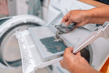 Dust and dirt trapped by the clothes dryer filter, female hand taking the lint out from dirty air filter of the dyer machine 