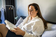 Focused overweight woman sitting at the bed at home involved at the reading interesting book
