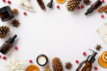 Winter Skin Care Concept. Top View Photo Of Amber Bottles Christmas Ornaments Pine Cones Mistletoe Berries Anise And Dried Orange Slices On Isolated White Background With Empty Space In The Middle
