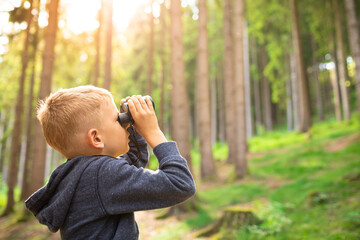 little boy in the woods exploring nature looking through binoculars at wildlife bird watching.