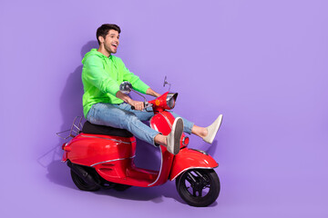 Sticker - Full length photo of cheerful carefree guy dressed green hoodie ride on motorcycle look empty space isolated on purple color background