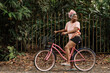 Imagen horizontal del perfil de una joven mujer afroamericana con cabello rosado en exterior dando un paseo en bicicleta en un día de verano. 