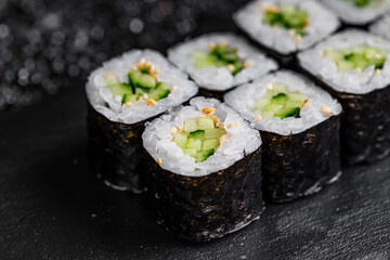 Canvas Print - Asian cuisine. Roll with cucumber on a black stone on a black background. rice nori cucumber sesame