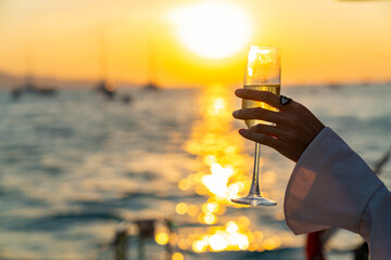 Caucasian woman hand holding champagne glass relax and enjoy luxury outdoor lifestyle while travel on catamaran boat yacht sailing in the ocean at sunset on summer beach holiday vacation trip