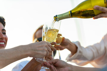 Wall Mural - Asian man waiter pouring and serving champagne to passenger tourist while catamaran yacht boat sailing in the sea at summer sunset. Man and woman enjoy luxury outdoor lifestyle on travel vacation.