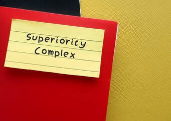 Red notebook on yellow background with handwritten text SUPERIORITY COMPLEX, means belief that your abilities or accomplishments are dramatically better than someone else