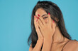 Portrait of yong happy ashamed woman, covering face with hands, beautiful model posing in studio over blue background. Caucasian portrait woman.