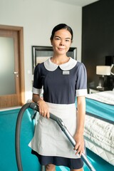 Poster - Photo realistic digital collage of young pretty chambermaid in uniform working with vacuum cleaner and looking at you