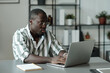 © pressmaster - Young serious man in eyeglasses and striped shirt looking at laptop screen while sitting by workplace and preparing presentation