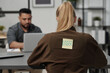 © pressmaster - Back of young blond businesswoman with word loser written on sticky notepaper sitting by workplace in front of Hispanic male colleague
