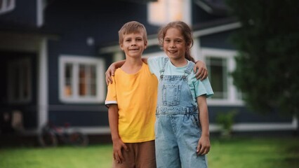 Wall Mural - Young Cheerful Siblings Posing Outdoors, Hugging and Looking at Camera and Smile. Two Boy and Girl Friends Standing on a Lawn in Front of Suburban House, Enjoying Summer Time, Childhood, Friendship.