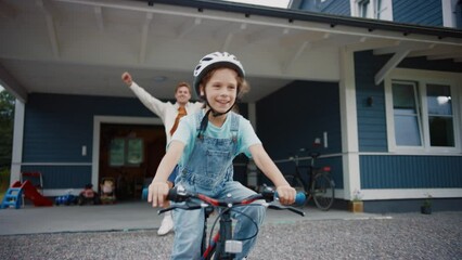 Wall Mural - Young Father Teaching His Daughter to Ride a Bicycle on the Lawn of Their Big Home. Successful Girl Wearing a Helmet, Balancing and Pedaling Herself on a Bike. Handheld Slow Motion Footage.