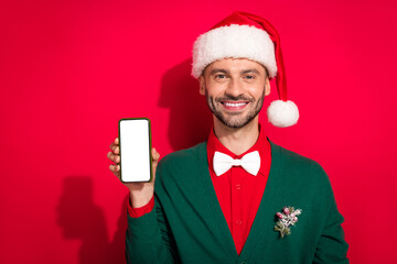 Wall Mural - Photo of positive cute man wear x-mas bowtie green cardigan rising apple samsung modern device empty space isolated red color background