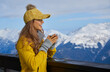 © ZoomTeam - Woman drinking warm tea in the rustic wooden terrace on mountain, alpine view, snow on hills.