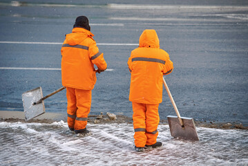 Utility workers cleaning snow with shovel, snow removal work. Workers team clear snowy walking path. Man with shovel shoveling snow from sidewalk after heavy snowfall in winter season.