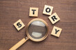 Magnifying glass with wood blocks of STORY word on woof background, finding a story idea
