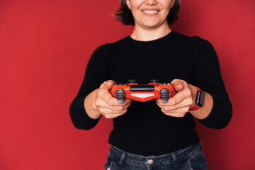 Wall Mural - Woman holding gamepad in her hands against red background.