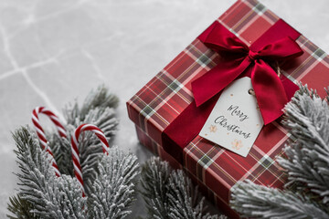 A red gift box, spruce branches, candy cane and a label with the inscription merry Christmas on a gray marble background. Christmas holidays 2023. Buying and preparing gifts for family and relatives.