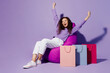 © ViDi Studio - Full body fun excited happy young woman in pullover sit in chair near paper package bags after shopping spread hand isolated on plain pastel light purple background Black Friday sale buy day concept