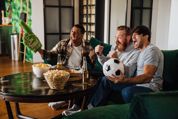 Canvas Print - Three men gesturing as winners while watching football at home