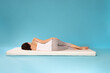 © New Africa - Young woman sleeping on soft mattress against light blue background, back view
