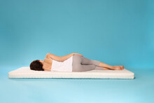 Young Woman Sleeping On Soft Mattress Against Light Blue Background, Back View
