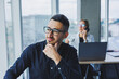 © Дмитрий Ткачук - Attractive business man of Caucasian appearance in a black shirt sits at a desk using a laptop in a modern office with colleagues in the background. Working atmosphere in the office.