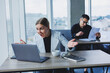 © Дмитрий Ткачук - A female manager is sitting at a desk using a laptop in a modern office against the background of a colleague. Working atmosphere in the office.