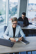 © Дмитрий Ткачук - Working atmosphere in an office with large windows. A female manager is sitting at a desk using a laptop in a modern office against the background of a colleague.