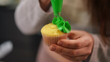 Close-up Female Hand Squeezing Green Icing From Piping Bag On Baked Cupcake In Slow Motion. Young Unrecognizable Plus-size Caucasian Woman Decorating Delicious Pastry Indoors