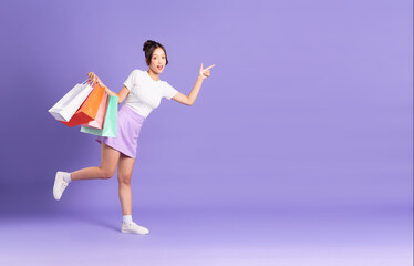 Young Asian woman holding shopping bag on purple background