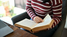 Asian Female College Student Reading A Book While Sitting In The Campus Library. Cropped Image