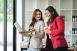 © Daenin - Two female designers smile at the camera as they work together at a conference room table during a meeting in a modern office. collaboration concept