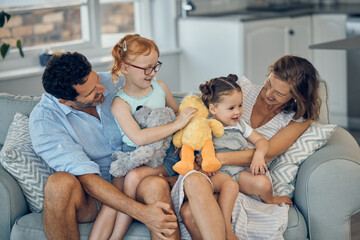 Canvas Print - Family, happiness and love on home sofa with children holding stuffed animal toys while bonding with mom and dad parents. Woman, man and girl kids together for care, development and quality time