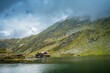 Beautiful view of Balea Lake and green mountain slope covered with clouds. Romania.