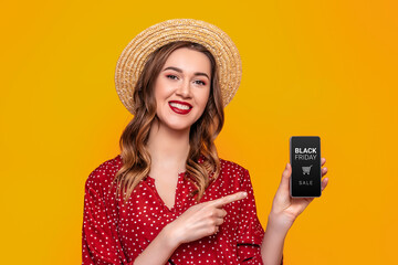 Wall Mural - Young woman showing mobile phone with black friday app isolated on orange background