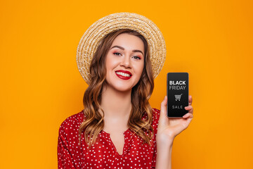 Wall Mural - Young woman showing mobile phone with black friday app isolated on orange background