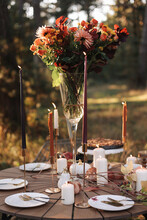 Cozy Autumn Picnic In The Park. Close Up Of Table Setting With White Plates, Cutlery, Glass Vase With Colourful Wildflowers, Homemade Apple Pie, Maple Leaves, Burning Candles On Wooden Table Outdoors.