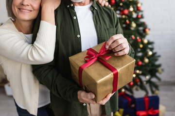 Wall Mural - cropped view of happy middle aged woman hugging husband with christmas present