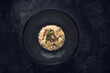 Black truffle risotto recipe.  Autumn creamy consistency risotto in stylish black dish on the black background. Dark autumn or winter mood in the style of the Chef's table, one dish