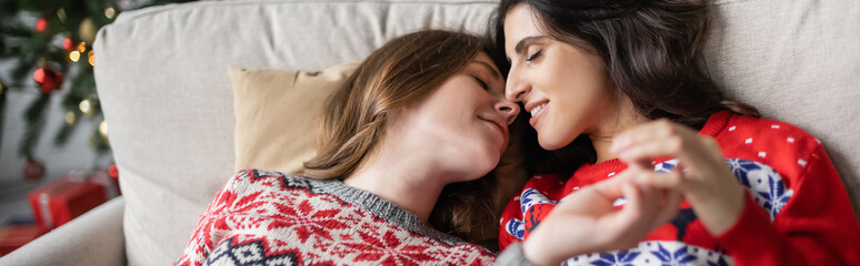 Sticker - Lesbian couple in christmas sweaters touching hands and kissing at home, banner